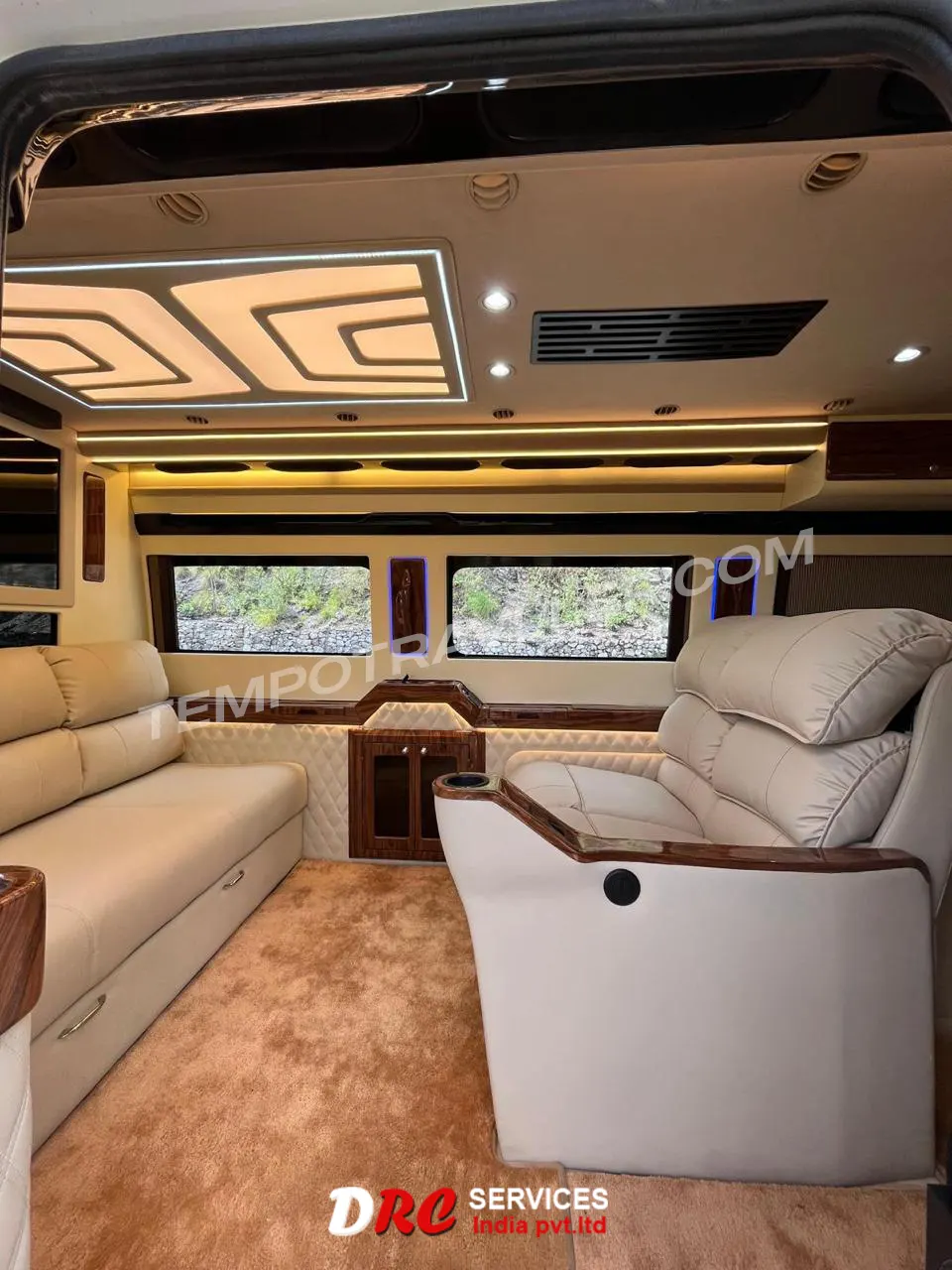 Spacious luxury motorhome lounge area with plush sofa seating, LED ceiling lights, wooden accents, and panoramic windows.